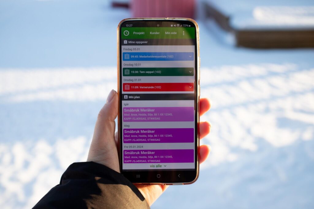 en hånd som holder en telefon, i bakgrunnen er det snø. På telefonskjermen visere Proresul-appen.